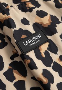 Tkanina z beżowo-brązowo-czarnym wzorem w panterkę oraz czarną prostokątną metką z napisem „LARKSON HAMBURG” przyszytą na niej.