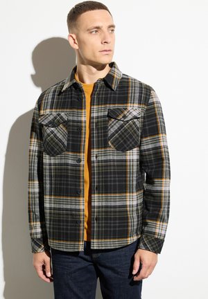 Camicia in flanella a quadri nera e grigia con accenti gialli, dotata di due tasche sul petto, chiusura con bottoni e colletto aperto.