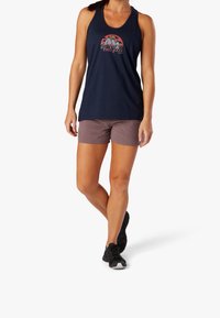 Canottiera blu navale con grafica di montagna, abbinata a pantaloni corti marroni. La canottiera presenta un design senza maniche, mentre i pantaloni corti hanno una vestibilità casual.