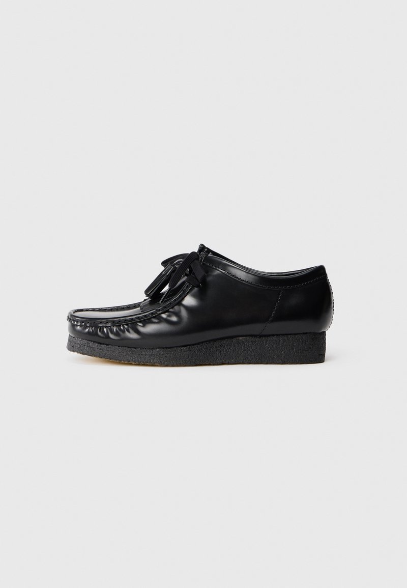 Sapatos de couro pretos com ponta arredondada, atacadores à frente e sola plataforma texturizada preta, apresentando costuras decorativas ao longo das bordas.