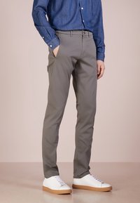 Šedé přizpůsobené kalhoty vyrobené z lehké látky, s rovný střih, bočními kapsami a pasem se smyčkami na opasek, doplněné o bílé tenisky.