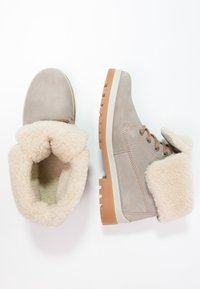 Beige Wildleder-Stiefeletten mit einem weichen cremfarbenen Futter und umgeschlagenem Schaft, ausgestattet mit braunen Gummisohlen und Metallösen für die Schnürsenkel.