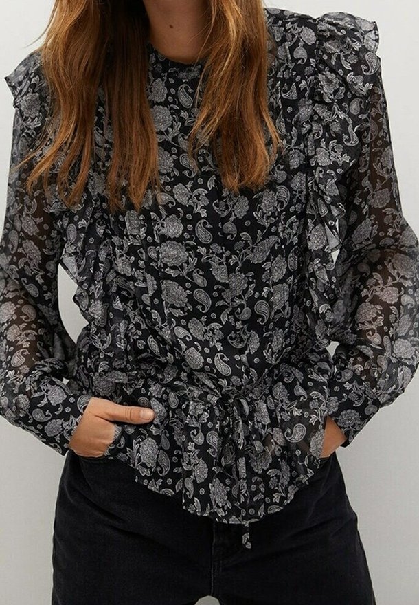 Blusa nera trasparente con motivo floreale paisley bianco, maniche a volant e vita con lacci. Presenta maniche lunghe e un design intricatamente dettagliato.