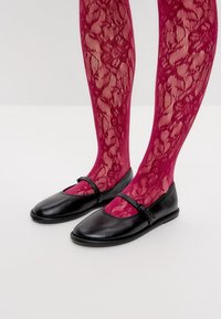 Bailarinas de cuero negro con punta redonda, que presentan una tira en la parte superior y se combinan con medias magenta de texturas y con un patrón floral.