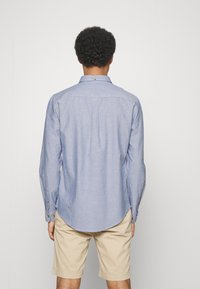 Camicia azzurro chiaro a maniche lunghe con collo button-down, orlo arrotondato, piega sul retro e polsini con bottoni, realizzata in un tessuto testurizzato. Abbinata a pantaloni corti beige.
