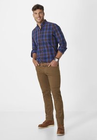 Blue and brown plaid shirt with long sleeves, paired with tan trousers and brown lace-up boots. Includes belt and watch accents.