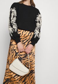 Pull noir avec broderie florale crème sur les manches, associé à une jupe dorée à rayures de tigre. Sac bandoulière beige avec quincaillerie dorée.