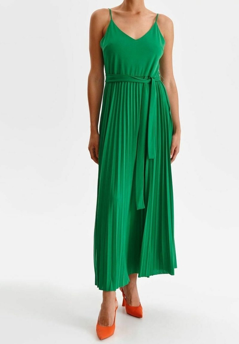 Grön maxiklänning med veck, justerbara smala band, figursydd midja och matchande knytbälte; kombinerad med orange högklackade skor.