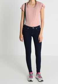 Light pink short-sleeve t-shirt paired with dark blue skinny jeans and gray athletic shoes. The outfit features a casual design with a slender fit.