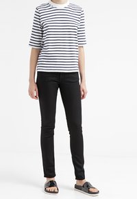 Camiseta de algodón a rayas en blanco con rayas horizontales en azul marino, combinada con jeans slim negros y sandalias negras con un diseño geométrico.