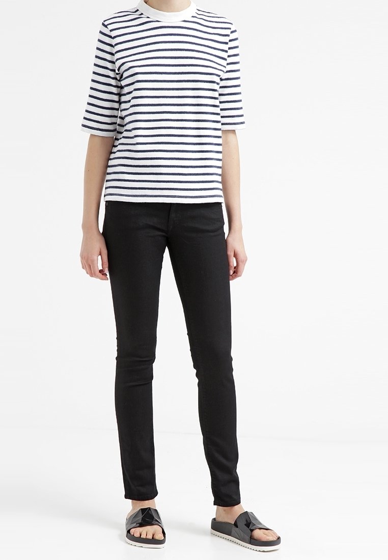 Camiseta de algodón a rayas en blanco con rayas horizontales en azul marino, combinada con jeans slim negros y sandalias negras con un diseño geométrico.