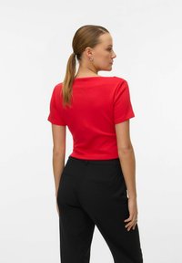 Top corto rojo de manga corta con escote redondo, textura suave, combinado con pantalones negros ajustados que cuentan con bolsillos laterales y un corte recto.