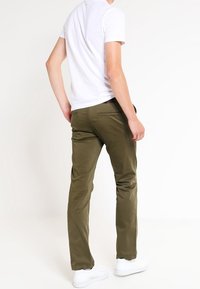 Olivgröna chinos med slim fit-design, tillverkade av lätt bomull. Har fickor och en mjuk textur. Kombination med en vit t-shirt.