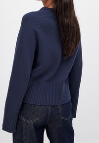 Granatowy dzianinowy sweter z prążkowanym ściągaczem u dołu i na mankietach, ozdobiony fakturowanym wzorem na plecach oraz z opadającymi ramionami.