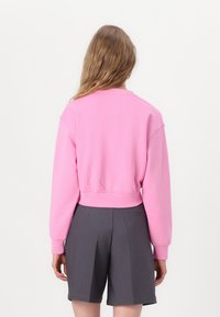 Rosa cropped genser med lange ermer, ribbestrikkede mansjetter og nederkant. Kombinert med grå skreddersydde shorts med lommer og feite detaljer.