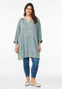 Mintgrön blus med V-ringning, lös passform och trekvartslånga ärmar med blommönster; matchas med blå denimjeans.