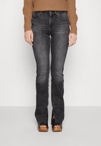 Donkergrijze jeans met een getailleerde taille, lichte flare aan de onderkant en details op de voorzakken. De stof heeft een gladde textuur en subtiele vervaging.