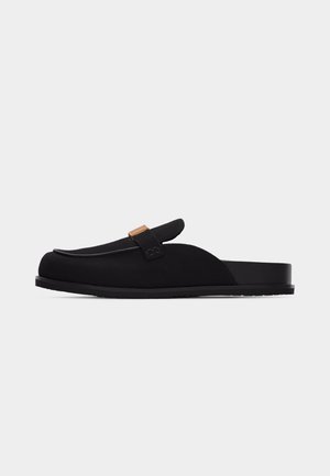 Juodų slip-on tipo batų su plokščiu padu ir dekoratyvia juostele su maža auksine sagtimi.