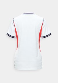 Λευκό πουκάμισο με κοντά μανίκια, κόκκινα πλαϊνά πάνελ και ριγέ λεπτομέρεια σε σκούρο μπλε στα μανίκια και το γιακά, εμφανίζεται από πίσω σε απλό φόντο.