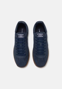 Zapatillas de tenis de ante azul marino con una textura suave, puntera redonda y suela de goma. Presentan un diseño de cordones y una marca en la lengüeta.