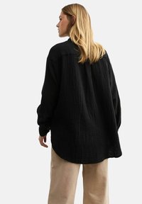 Zwarte textuur lange mouwen shirt met een losse pasvorm, met een ronde zoom en knoopmanchetten, gedragen met beige broeken.