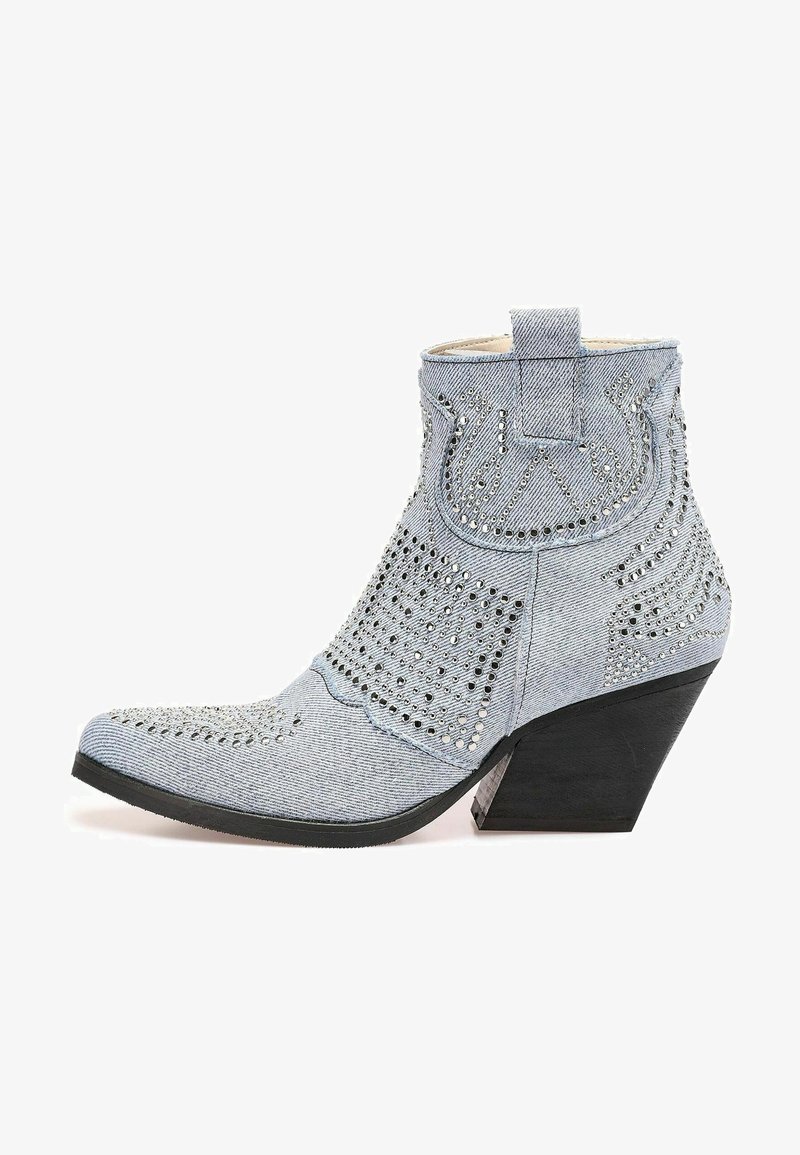 Stivale alla caviglia in denim blu chiaro con punta affusolata, superficie texturizzata, tagli decorativi e borchie argentate. Presenta un tacco a zeppa nero.