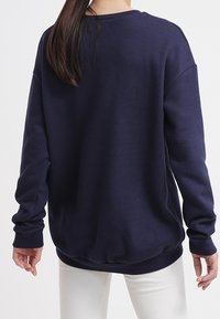 Felpa blu navy realizzata in tessuto morbido, con colletto rotondo, maniche lunghe e orlo a coste, mostrata da dietro.