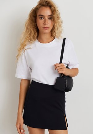 T-shirt branca de algodão com mangas curtas, combinada com uma saia mini preta com uma fenda lateral, e uma pequena mala cruzada preta.