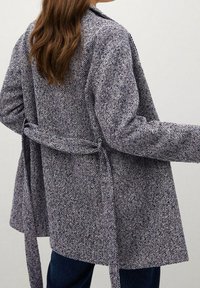 Cappotto blu e bianco a scacchi houndstooth con tessuto testurizzato, apertura frontale, maniche lunghe e dettaglio fascia in vita. Visuale dalla parte posteriore.