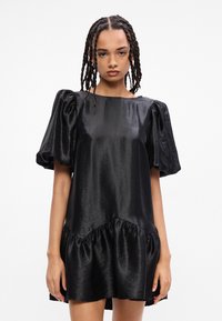 Μαύρο σατέν φόρεμα με κοντά φουσκωτά μανίκια, δομημένο μπούστο και ριχτό στρίφωμα. Μοναδική υφή με διακριτική γυαλάδα.