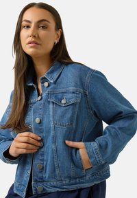 Jeanjacka i medelblå med en klassisk design, med knappstängning framtill, bröstfickor och en avslappnad passform med sidfickor.