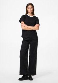 Must t-särk mustade lühikeste varrukatega, valge ümar kaelusega, koos kõrge vöökohaga mustade laiade pükste ja mustade paksude saabastega.