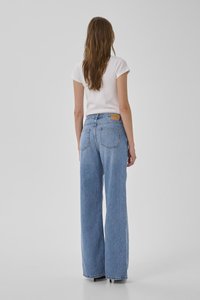 Atsipalaidavusio silueto, aukštu liemeniu šviesiai mėlyni džinsai su plačiomis kojomis, jie turi diržo kilpas, nugarinius kišenes ir šviesiai rudos odos etiketes nugarinės juostos zonoje.