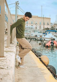Pantaloni cargo beige e un maglione di lana verde, con scarpe da ginnastica multicolori caratterizzate da una base azzurro chiaro e un prominente design di stella grigia.