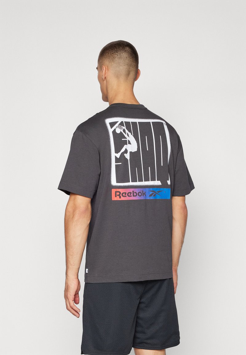 Tmavě šedé bavlněné tričko s velkým bílým grafikou basketbalisty na zadní straně a barevným logem Reebok ve spodní části.