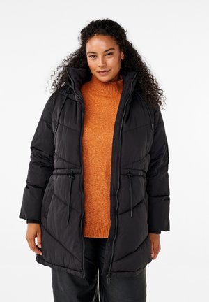 Zwarte gevoerde jas met een capuchon, voorzien van een rits en trekkoorddetails. Draag over een oranje coltrui. Soepele textuur.