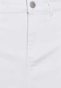 Bílá džínová látka na detailu zobrazující kovový knoflík na pásku a jemné švy podél švu a kapes.