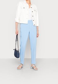 Pantaloni su misura azzurri, giacca in denim bianca, top bianco e sandali azzurri. Piccola borsa scura con dettagli a catena. Tessuti lisci.