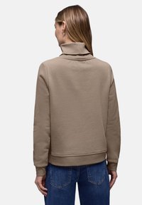 Sweat-shirt beige avec un col montant, un ourlet et des poignets côtelés, associé à un jean bleu. Le tissu semble doux avec une texture lisse.