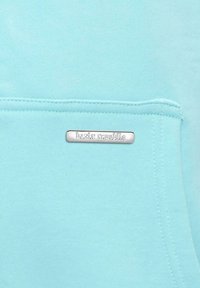Tessuto di felpa azzurro chiaro con una morbida texture, dotato di una tasca frontale e di una placca d'argento etichettata "basic republic."