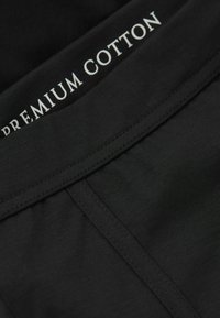 Svart bomullstyg med en slät textur; har en bred midjeband märkt "PREMIUM COTTON" i vit text.