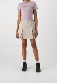 Ljuslila kortärmad t-shirt med "TERREX" tryck; beige veckad kjol; svarta vandringskängor. Bomullsmaterial med en slät yta.