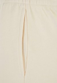 Joggeurs de couleur crème en coton doux, dotés d'une fente latérale pour la ventilation et d'une taille élastique pour le confort.