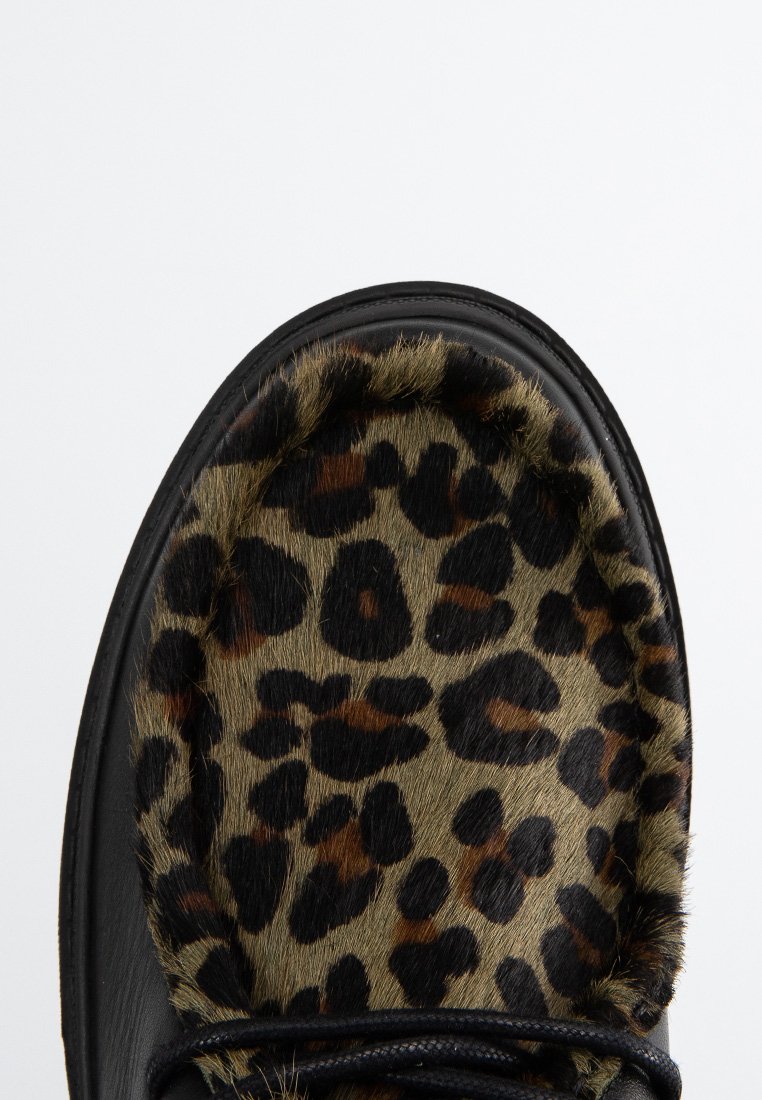 Chaussure noire avec un dessus en fourrure à imprimé léopard, présentant une fourrure texturée et un bout rond, complétée par des lacets noirs et une semelle lisse.