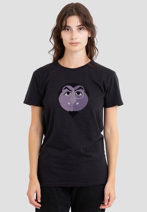 Schwarzes Baumwoll-T-Shirt mit einem lila, cartoonhaften Gesichtsgrafik, die auffällige Augenbrauen und Fangzähne zeigt, zentral präsentiert.