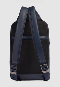 Mochila azul marina hecha de tela texturizada con detalles en cuero liso. Cuenta con correas ajustables y herrajes en tono plateado. Diseño minimalista.