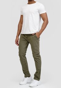 Vaaleanharmaa pyöreäkauluksinen T-paita yhdistetty oliivinvihreisiin slim fit -housuihin, joissa on etutaskut ja teksturoitu kangas. Valkoiset lenkkarit viimeistelevät asun.