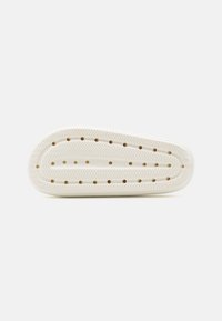 Shoe sole in off-white rubber with a textured herringbone pattern, featuring ventilation holes and an elongated oval shape.
