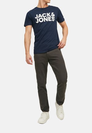 Marineblaues Baumwoll-T-Shirt mit weißem "JACK & JONES"-Logo, kombiniert mit dunkelgrauen Hosen und weißen Sneakern, die ein lässiges Outfit zeigen.