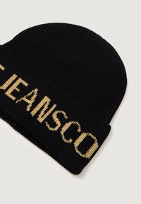 Melnā adītā beanie cepure ar zeltīti izšūtu tekstu. Ribota tekstūra un pieguļoša forma, kas piemērota ikdienišķai nēsāšanai.